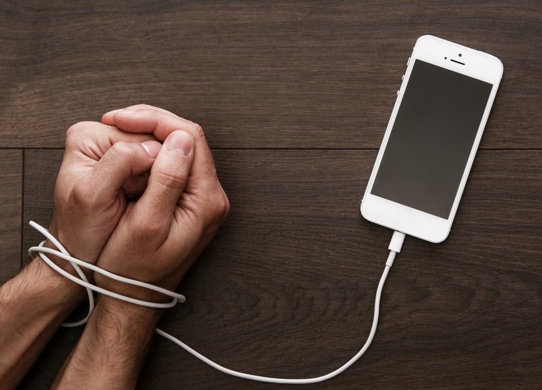 Mani legate al cavo dello smartphone, simbolo della dipendenza da telefono